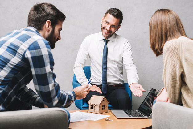 Agent immobilier en rendez-vous avec un couple de clients autour d’une maquette de maison